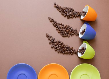 Kahverengi arkaplanda kahve çekirdekleri ve fotokopi alanı olan renkli kahve fincanları. Kahve konsepti. Üst görünüm.