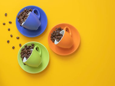 Fotokopi alanı olan sarı arkaplanda kahve çekirdekleri olan renkli fincanlar. Kahve konsepti. Üst görünüm.