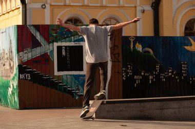 Şık giyinmiş gençler parkta kaykaya biniyorlar..