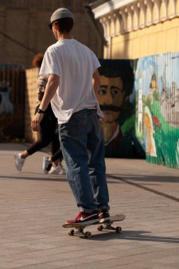 Şık giyinmiş gençler parkta kaykaya biniyorlar..