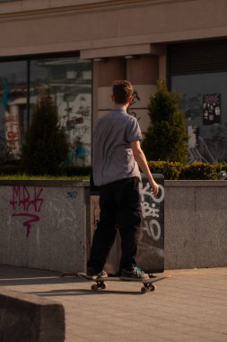 Şık giyinmiş gençler parkta kaykaya biniyorlar..