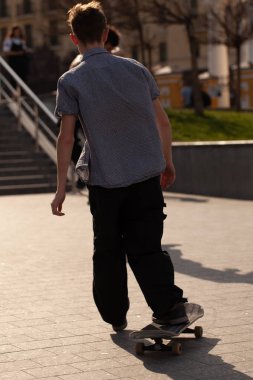 Şık giyinmiş gençler parkta kaykaya biniyorlar..