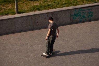 Şık giyinmiş gençler parkta kaykaya biniyorlar..