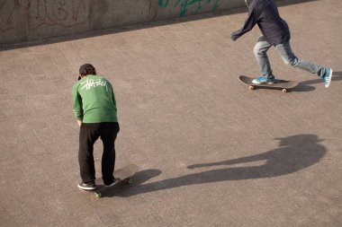 Şık giyinmiş gençler parkta kaykaya biniyorlar..