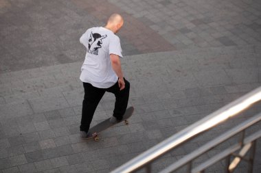 Şık giyinmiş gençler parkta kaykaya biniyorlar..