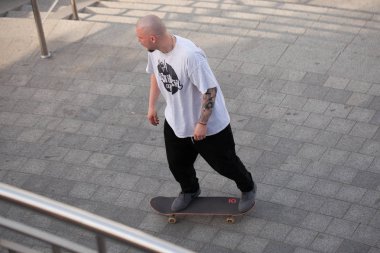 Şık giyinmiş gençler parkta kaykaya biniyorlar..