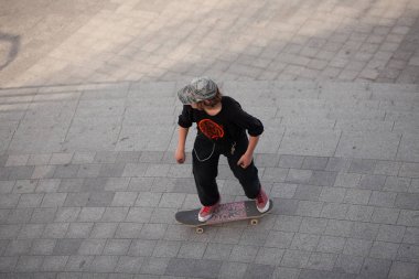 Şık giyinmiş gençler parkta kaykaya biniyorlar..