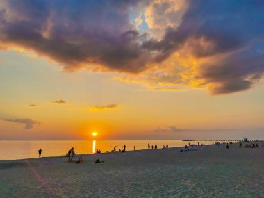 Sahilde gün batımının önünde bir grup insanın manzarası.
