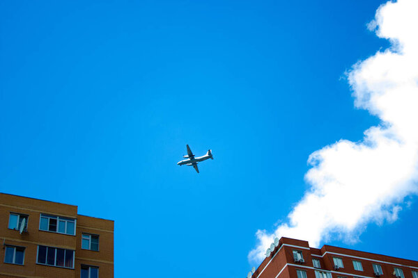 Turboprop plane flying between two houses against a blue sky with clouds.
