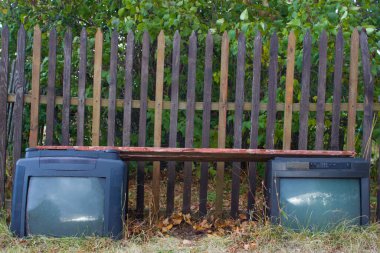 Çitin yanında duran iki eski televizyondan oluşan bir bank.. 