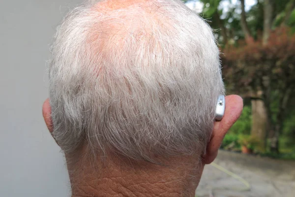 Deaf senior citizen man wearing modern digital high technology hearing aid in ear back view