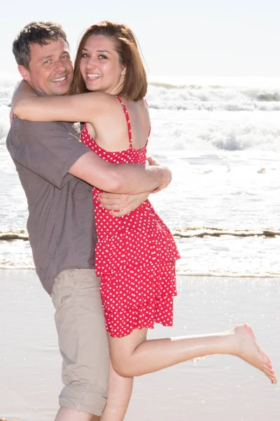 快乐的情侣在海滩上的爱有乐趣举行周围拥抱看相机 — 图库照片