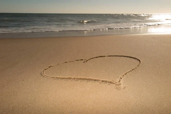 Summer holiday concept heart handwritten on a sand of beach with wave on background
