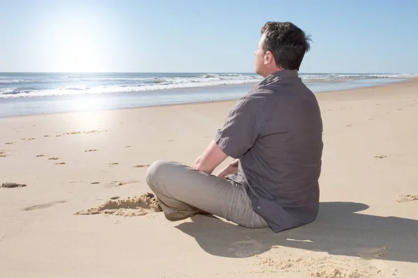 リラックス晴れた日に海で砂の上に座る一人の男 — ストック写真