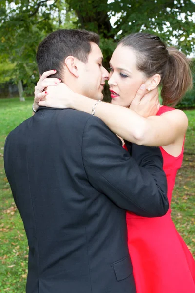 优雅的女人穿着红色的礼服倚在她的情人拥抱男人的爱概念 — 图库照片