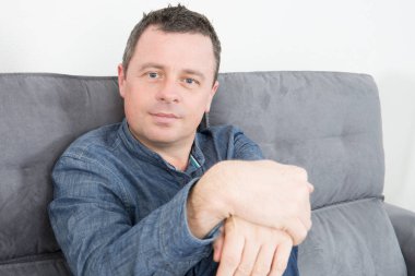 Yakışıklı bir adam portresi kanepe ev kanepe kameraya bakarak oturmak