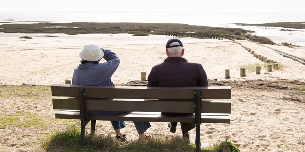坐在长椅上看海边的资深退休老人夫妇 — 图库照片