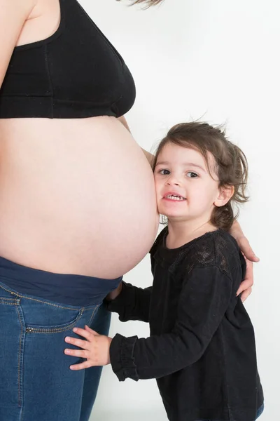 子供の女の子の最初の娘が妊娠中の母親の腹を聞く — ストック写真