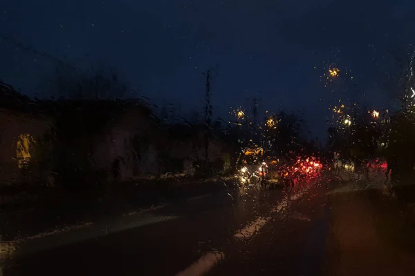 Wet car window with the background of the night city traffic rain fall at night with blurry cars