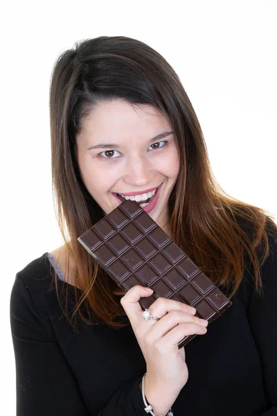 手をかむと白い壁の背景に分離したチョコレート バーを食べる黒セーターで笑いの若い女性 — ストック写真