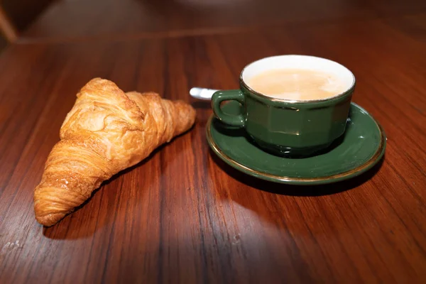 Morning coffee in green cup on wood table with croissant