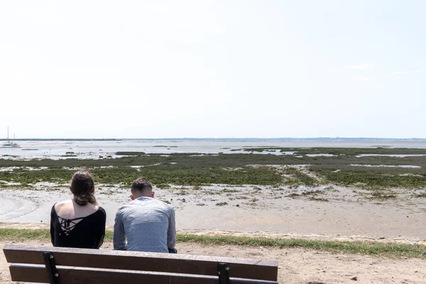 男人和女人夫妇坐在沙滩上 看着平静的低潮海 — 图库照片