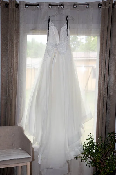 窓の前にぶら下がっている白いウェディングドレス — ストック写真