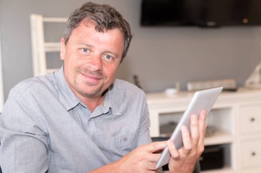 evde internette sörf yapmak için oturma odası pedtablet bilgisayar kullanarak kanepede oturan adam