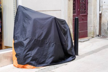 Motosiklet, koyu gri turuncu tente ceketli, sokak motorsikletinin koruması altında.