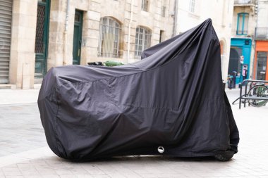 Motosiklet, üzerinde muşamba ceket olan bir motosikletle korunuyor.