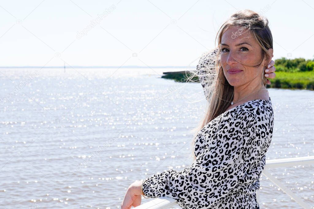 Young beautiful smiling woman with wind in hair standing at sea side with copy-space in outdoor shot