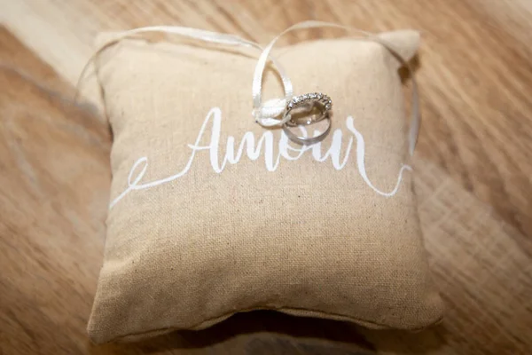 结婚戒指配上天然褐色小枕头 上面有彩带和情色文字 意思是在木制桌子背景上用法语表达爱情 — 图库照片