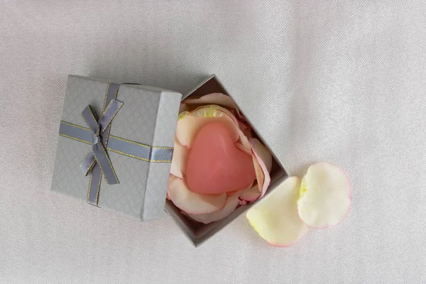 Grey gift box with rose petals and heart on a light beige background