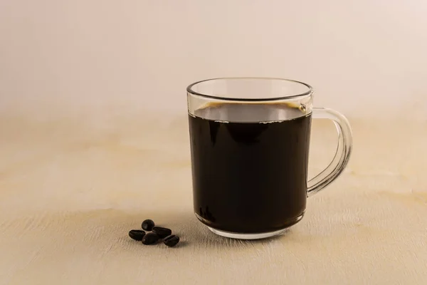 Black coffee with a delicate foam and grains close-up on a light wooden background