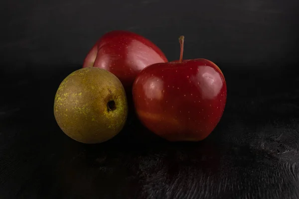 Two red apples and a pear on a dark wooden background