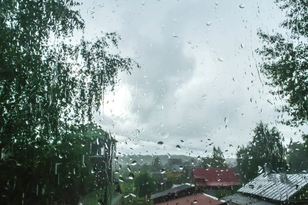 raindrops on the window. small houses and tree foliage. roofs of houses. gray sky and clouds