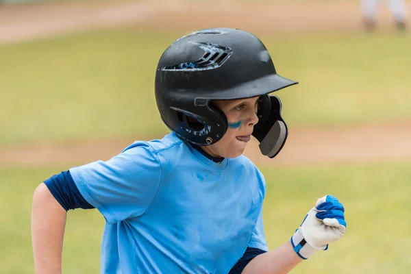 Close up of little league baseball players face showing eye black and concentration heading to first base.