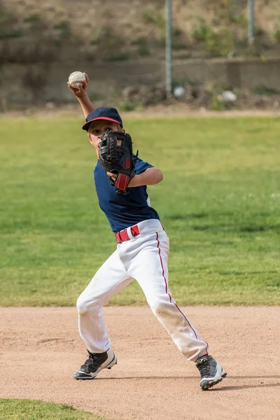 Little league short stop baseball player has arm loaded and ready to throw the ball across the diamond.