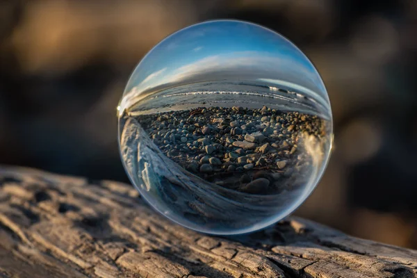 在纹理浮木上球形透镜扭曲的海滩鹅卵石海岸线 — 图库照片
