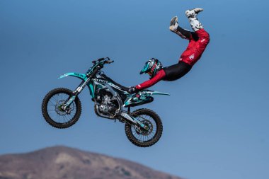 Stunt rider in red costume hangs on to seat of motorcycle while flying across the sky on jump during Flying U Rodeo at Ventura County Fair on August 12, 2018 in California. clipart