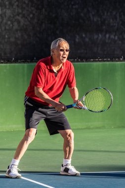 Çinli yaşlı adamın büyüttü raket ile hazır ve tenis bir oyun sırasında ciddi ifade odaklı.
