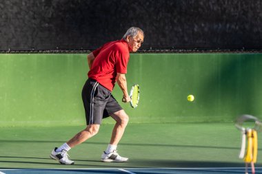 Yaşlı Çinli tenis bir oyun sırasında bir backhand vurmaya hazırlanırken göz topa tutmak duruldu.