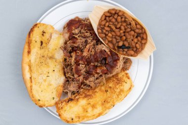 Overhead view of BBQ meal of pulled pork, baked beans, and butter toasted bread will taste as delicious as it looks. clipart