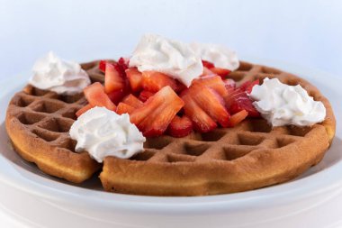 Yuvarlak tabakta çırpılmış kremayla süslenmiş doyurucu bir çilekli waffle..
