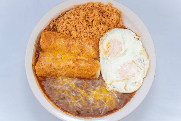 Вид сверху на щедрое питание сытной пары энчилад на завтрак в сочетании с пережаренной фасолью, рисом и яйцами.