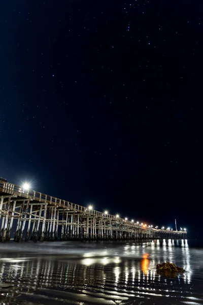 湿った砂の中の波紋のテクスチャは 上の空の星座の星とベンチュラ桟橋の下の海の水に反射するランプとして — ストック写真