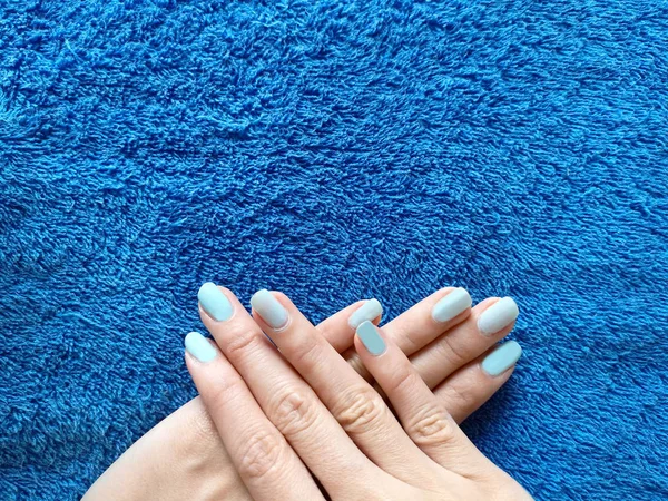 Beautiful Blue Manicure in Light. Close Up Nail Holding A Blue Fabric. Young Woman is Hand with Cyan Nails on Blue Textured Background.