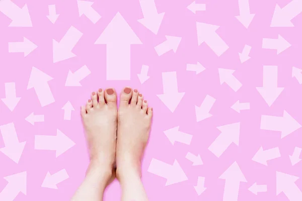 Pastel Arrow Choice Different. Woman Bare Feet with Pink Nail Polish Manicure Standing and Many Direction Arrows Choices on Pink Color Pastel. Female Fashion with Beautiful Legs and Feet on Background