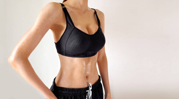 Fitness Exercise Sport Young Woman in Fashion Sportswear. Cropped Closeup of the Sexy Boobs Girl, Muscular Body, Tan Skin and Strong Six Pack Abs. Female Wearing Black Sports Bra on Grey Background.