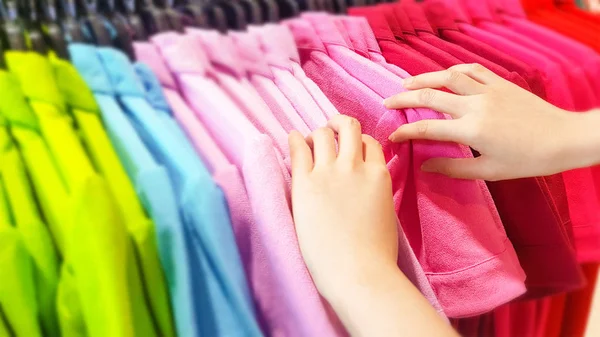 Buying Clothes in A Shopping Mall Store. Close Up of Woman Hand Choosing and Discount Colorful T-Shirt on Hanger in Store. People Standing to Finding or Searching a New Cotton Shirt. Fashion Concept.